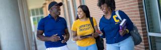 Three students talk outside of a building on campus